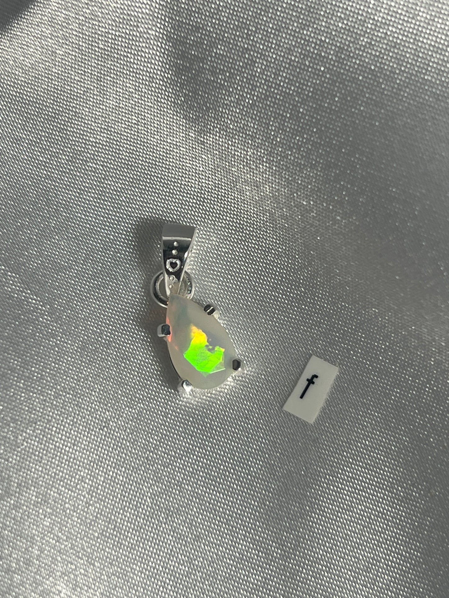 
                  
                    A Super Silver Dainty Prong Set Facet Cut Teardrop Shaped Ethiopian Opal pendant on a Sterling Silver surface.
                  
                