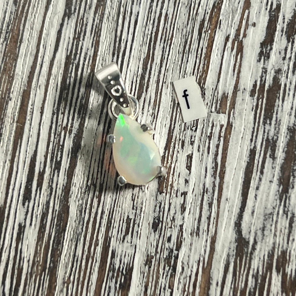 
                  
                    A Dainty Prong Set Facet Cut Teardrop Shaped Ethiopian Opal pendant by Super Silver on a wooden table.
                  
                