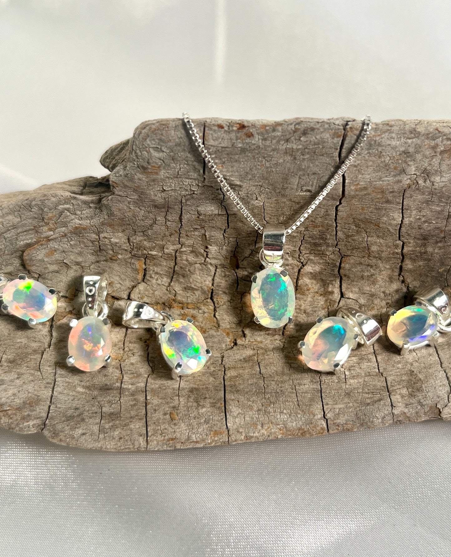 Super Silver's Tiny Facet Cut Prong Set Ethiopian Opal Pendant necklace and earrings on a piece of wood, made with .925 sterling silver.