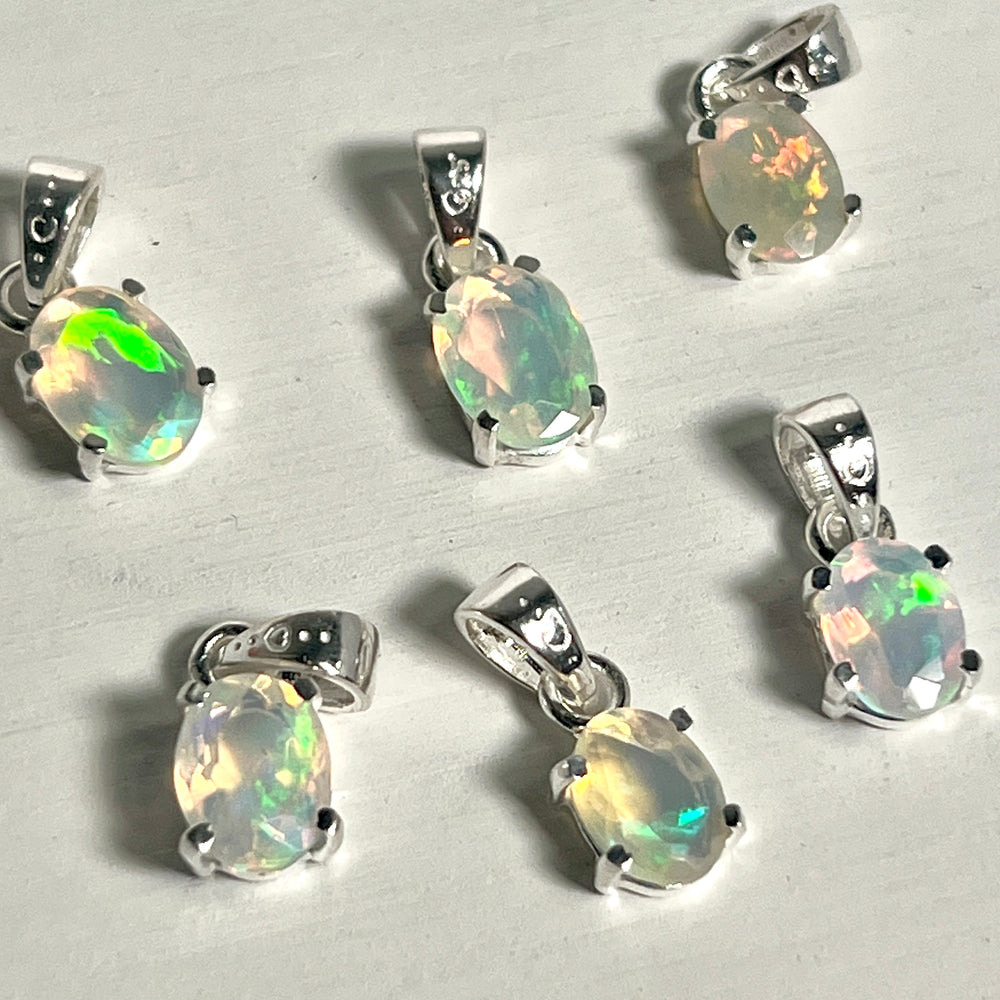 
                  
                    Six Super Silver Tiny Facet Cut Prong Set Ethiopian Opal Pendants on a dainty white table.
                  
                