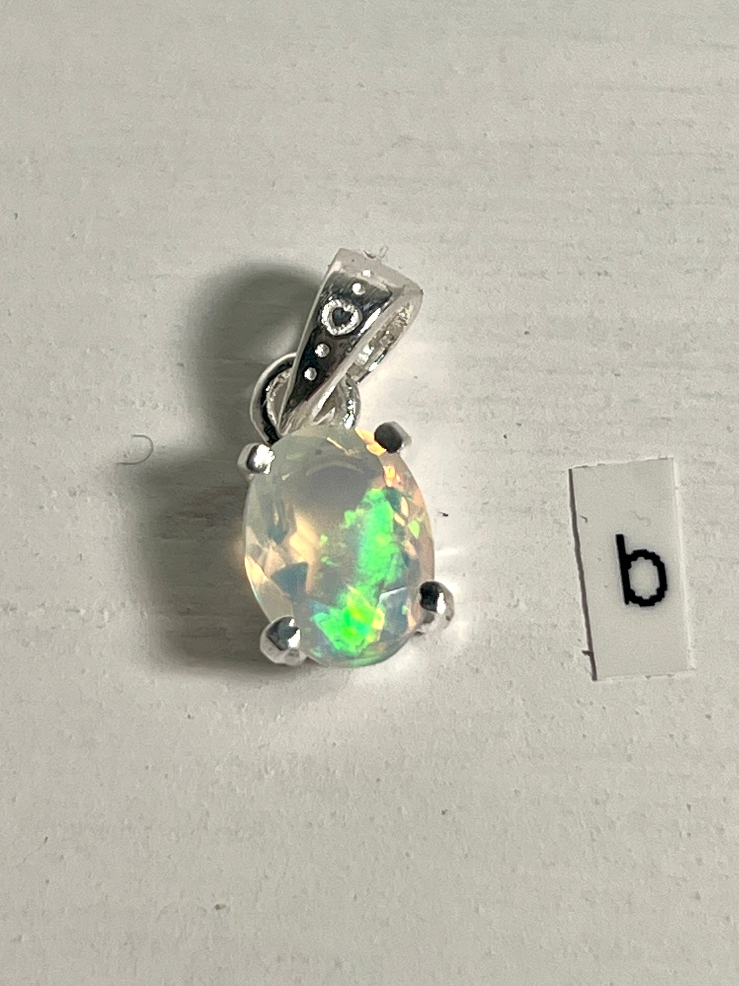 
                  
                    A Tiny Facet Cut Prong Set Ethiopian Opal Pendant by Super Silver with the letter B intricately engraved on it.
                  
                