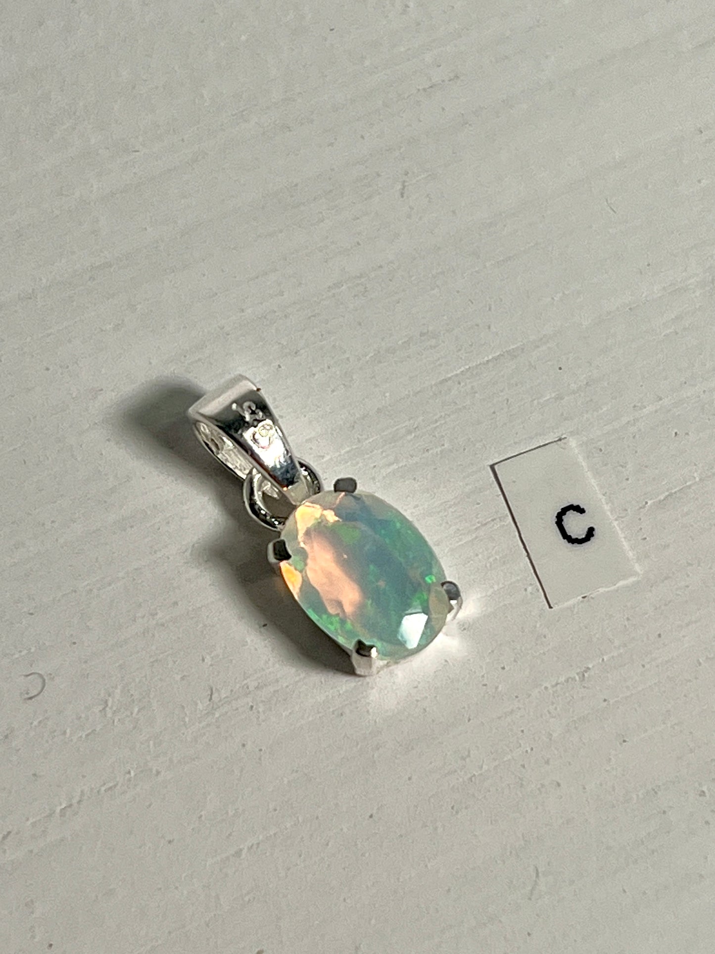 
                  
                    A dainty pendant made by Super Silver, featuring a Tiny Facet Cut Prong Set Ethiopian Opal and the letter c.
                  
                