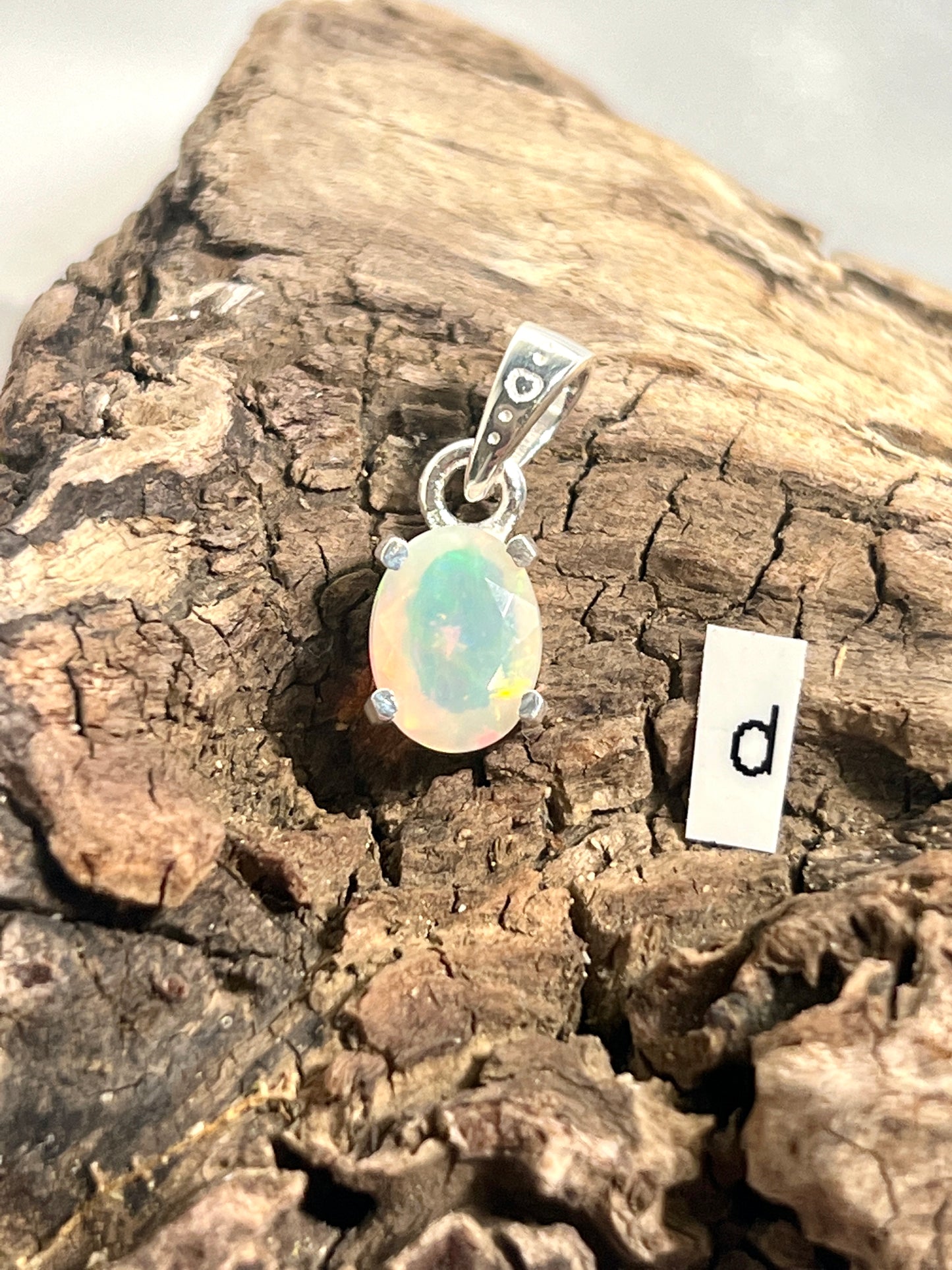
                  
                    A dainty Super Silver Tiny Facet Cut Prong Set Ethiopian Opal Pendant with the letter D intricately engraved on it.
                  
                