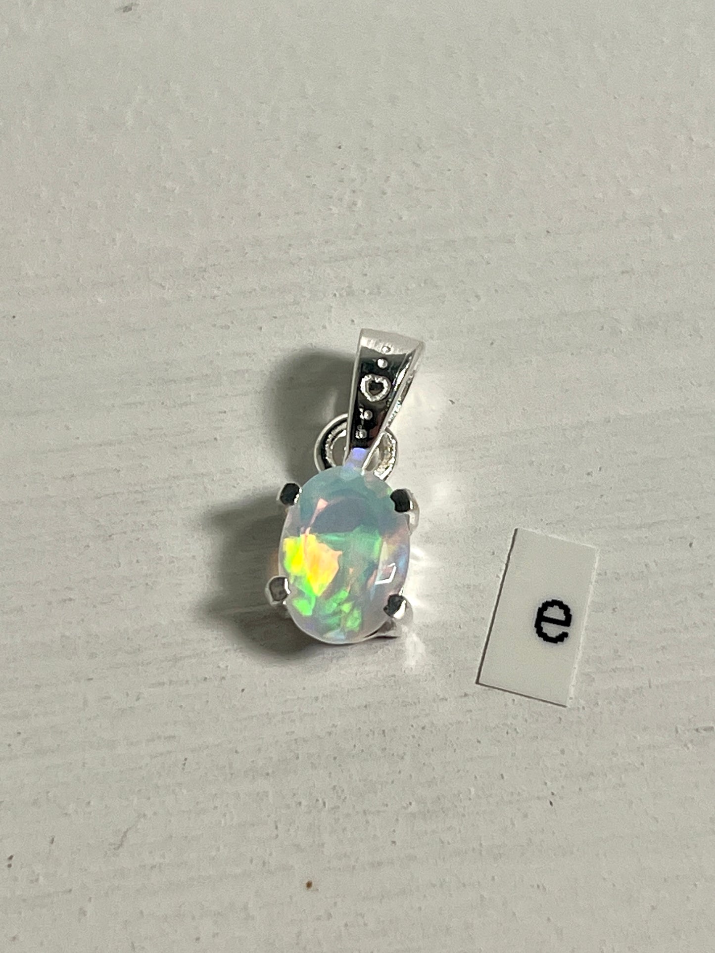 
                  
                    A dainty Tiny Facet Cut Prong Set Ethiopian Opal Pendant with the letter e, crafted in .925 sterling silver from Super Silver.
                  
                