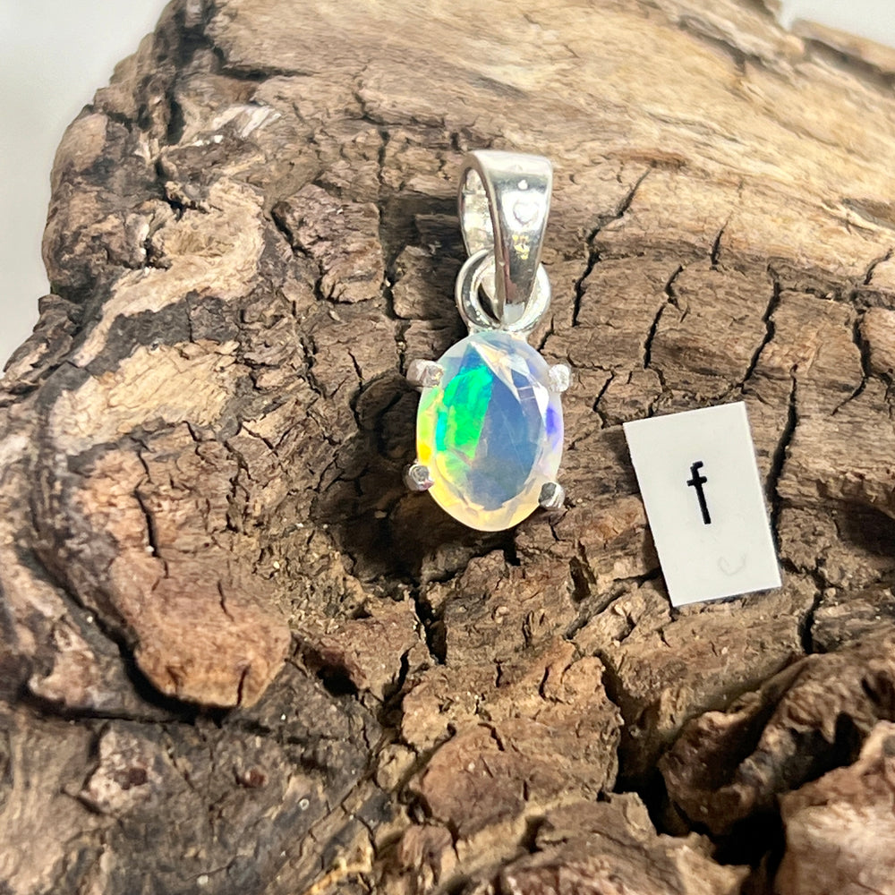 
                  
                    A Tiny Facet Cut Prong Set Ethiopian Opal Pendant by Super Silver on a piece of wood.
                  
                