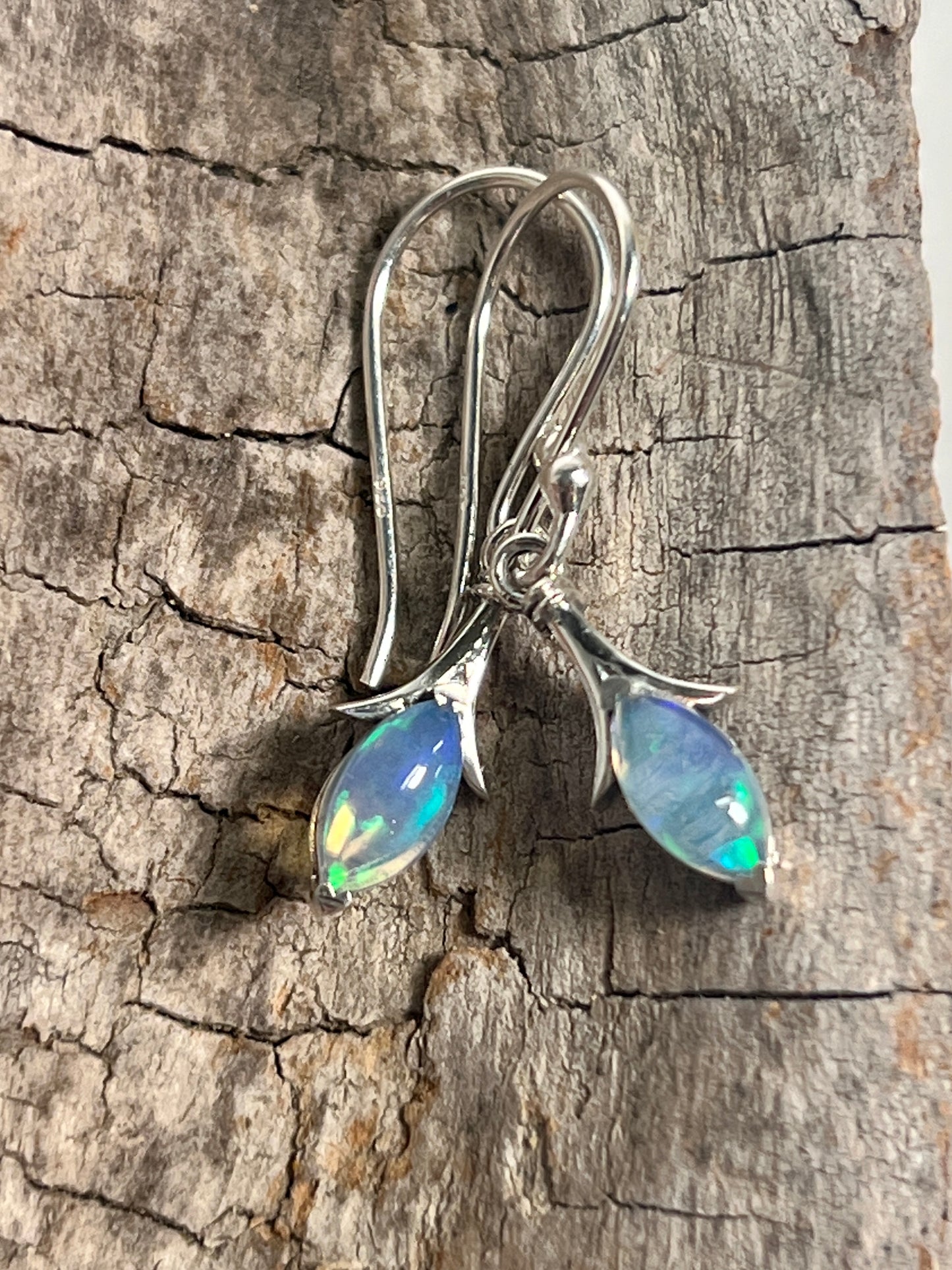 A pair of Modern Marquise Shaped Ethiopian Opal Earrings made with Ethiopian opal pieces, beautifully displayed on a piece of wood, by Super Silver.