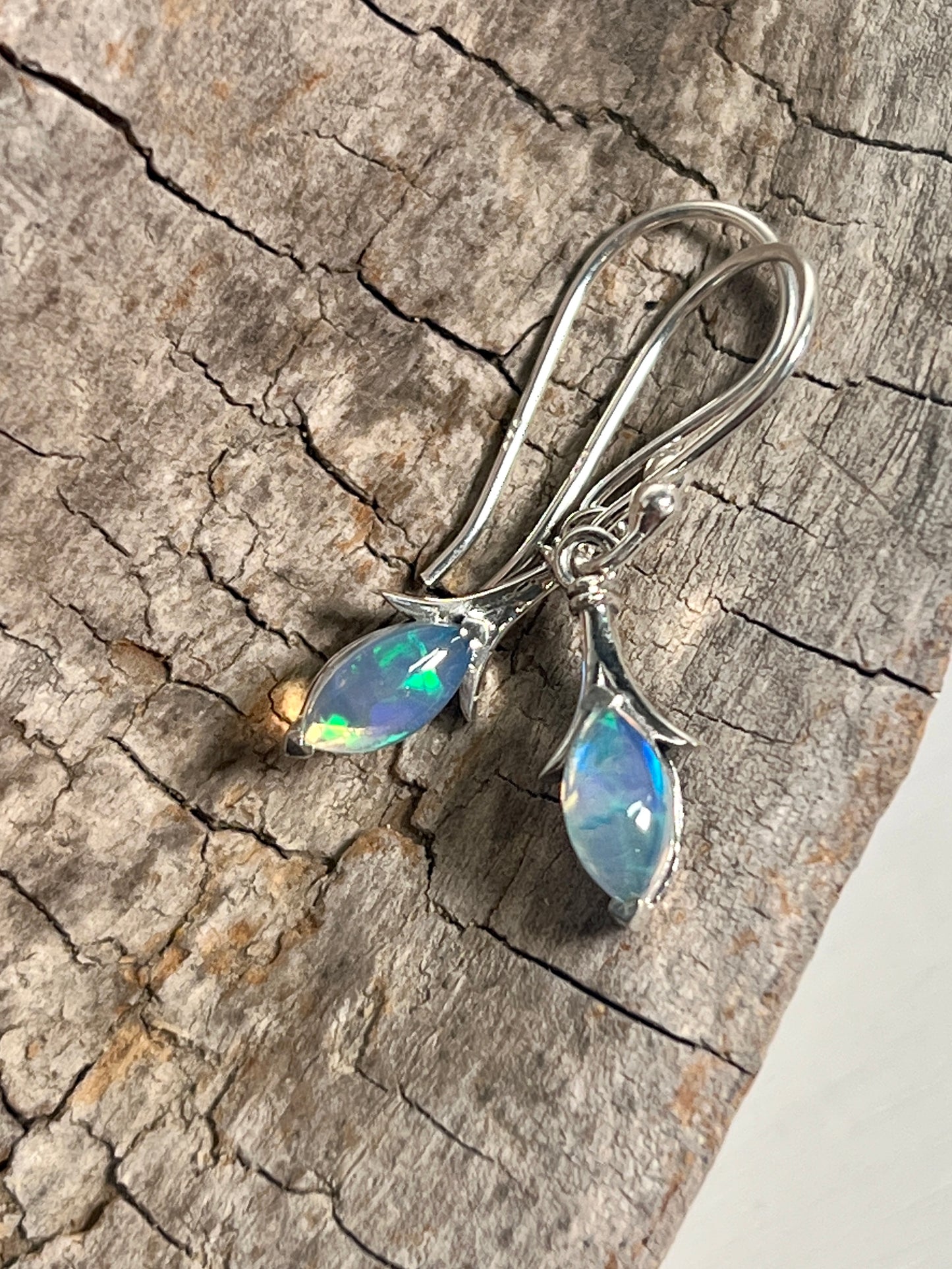 A pair of dainty Modern Marquise Shaped Ethiopian Opal earrings from Super Silver resting on a piece of wood.