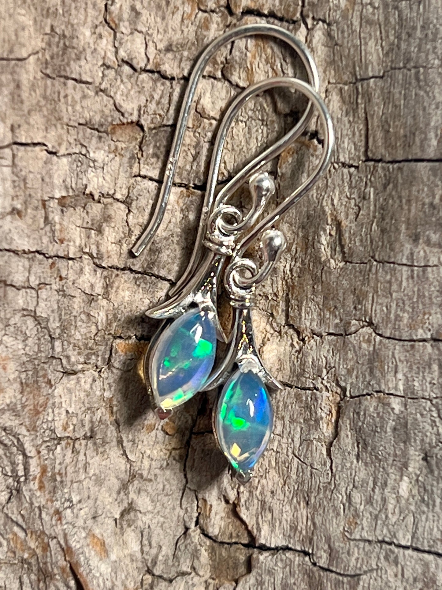 
                  
                    A pair of Modern Marquise Shaped Ethiopian Opal earrings by Super Silver on a piece of wood.
                  
                