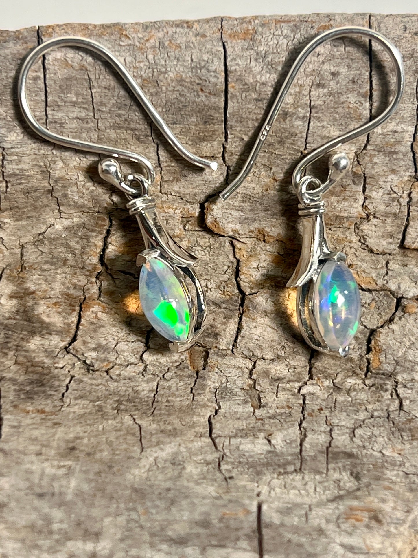 
                  
                    A pair of dainty Modern Marquise Shaped Ethiopian Opal Earrings by Super Silver on a piece of wood.
                  
                