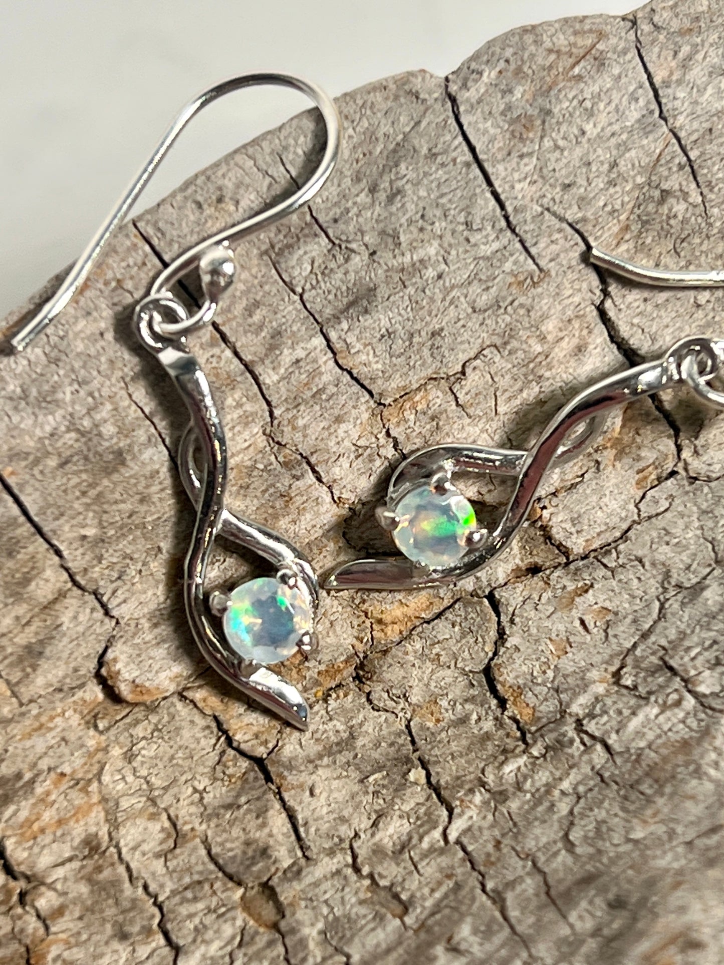 
                  
                    A pair of Super Silver Modern Ethiopian Opal earrings on a piece of wood.
                  
                