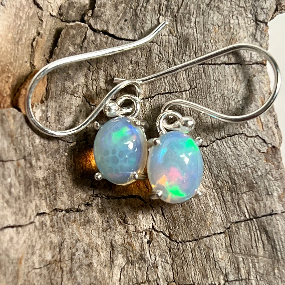 A pair of Vibrant Oval Ethiopian Opal Earrings from Super Silver, exuding natural brilliance on a piece of wood.