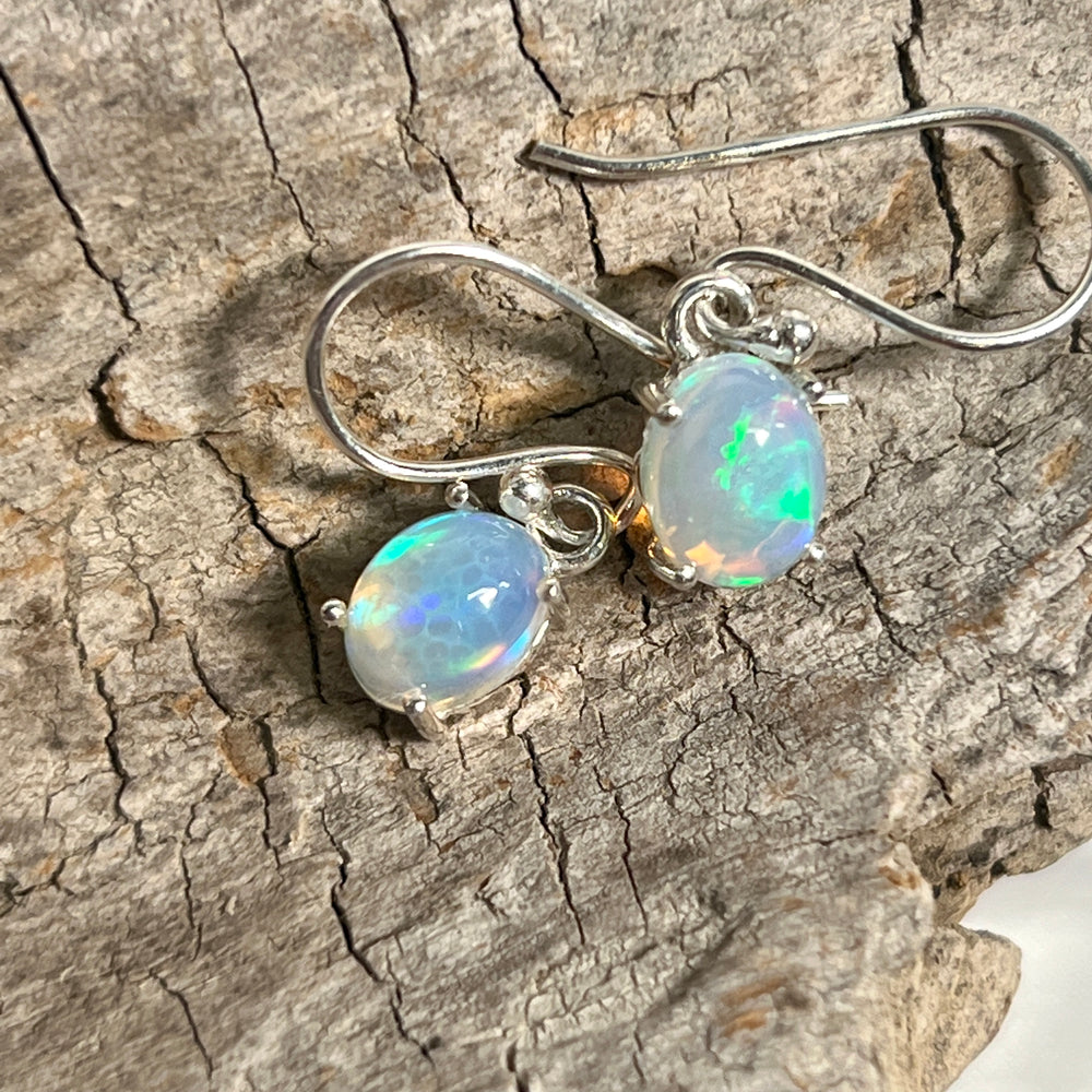 
                  
                    A pair of Super Silver Vibrant Oval Ethiopian Opal Earrings, with vibrant hues and natural brilliance, delicately displayed on a piece of wood.
                  
                