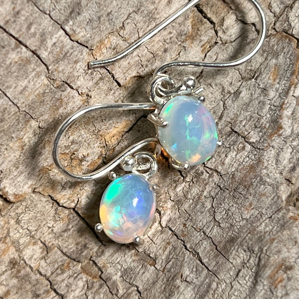 
                  
                    Super Silver Vibrant Oval Ethiopian Opal Earrings with natural brilliance on a piece of wood.
                  
                