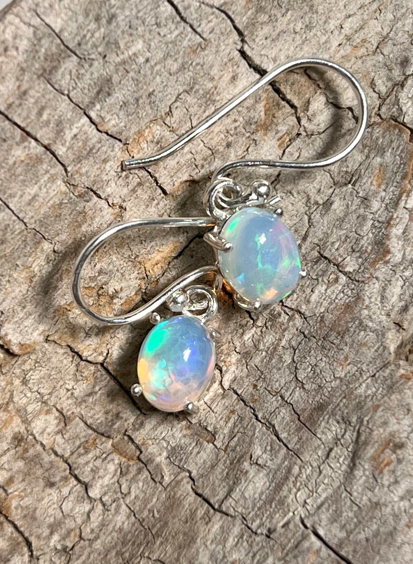 
                  
                    Super Silver Vibrant Oval Ethiopian Opal Earrings with natural brilliance on a piece of wood.
                  
                