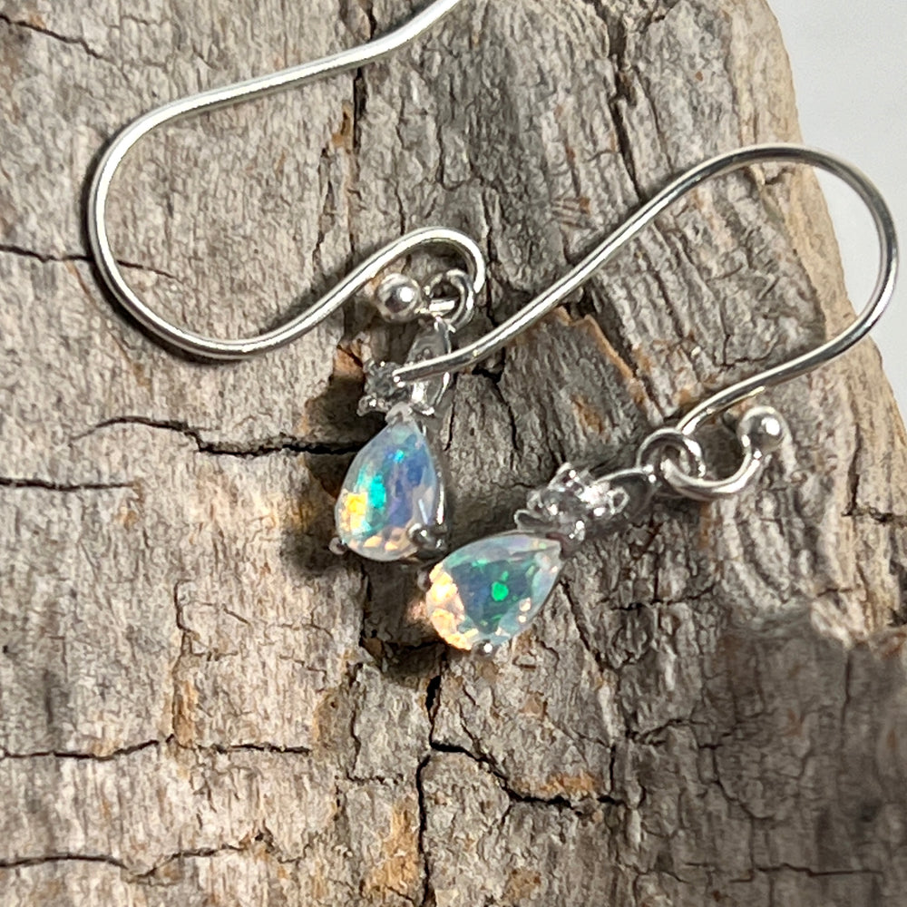 A pair of Super Silver Tiny Teardrop Ethiopian Opal earrings on a piece of wood.