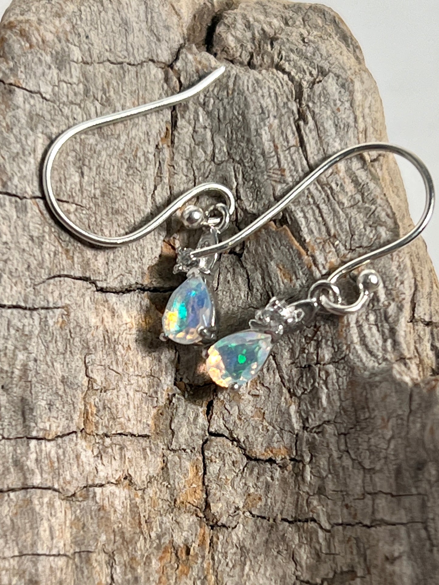 A pair of Super Silver Tiny Teardrop Ethiopian Opal earrings on a piece of wood.