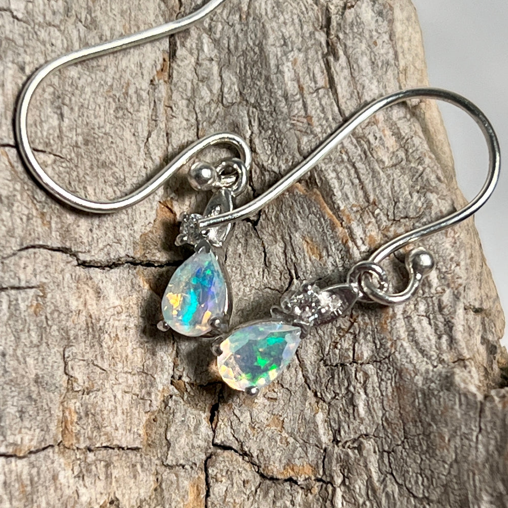 
                  
                    A pair of Tiny Teardrop Ethiopian Opal Earrings sparkling on a piece of wood, by Super Silver.
                  
                