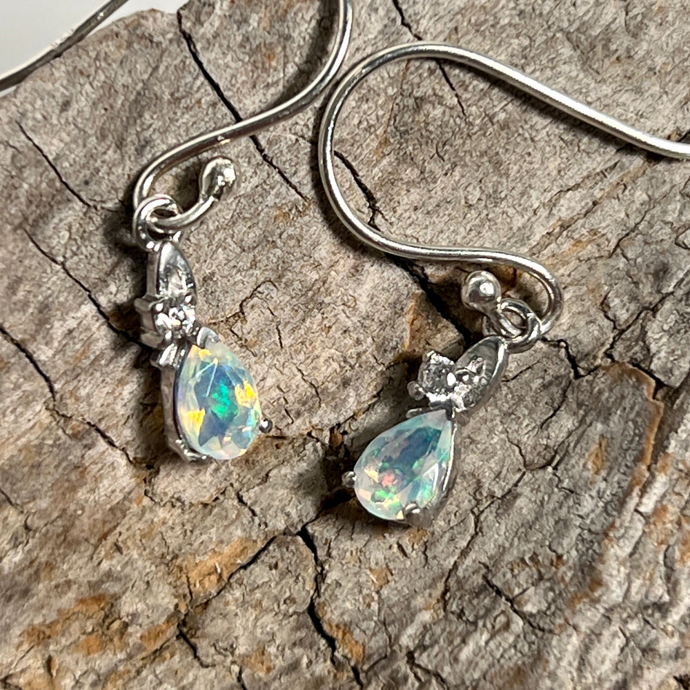 
                  
                    A pair of Tiny Teardrop Ethiopian Opal Earrings from Super Silver with a sparkle on a piece of wood.
                  
                