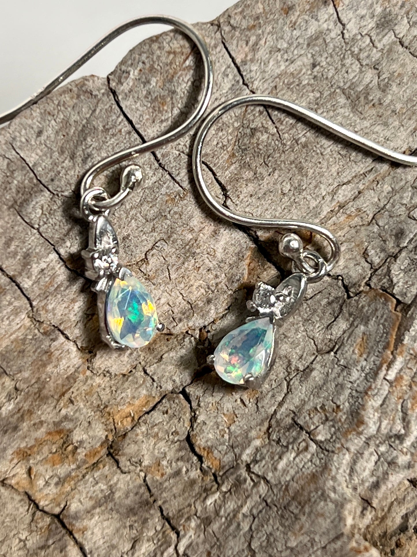 
                  
                    A pair of Tiny Teardrop Ethiopian Opal Earrings from Super Silver with a sparkle on a piece of wood.
                  
                