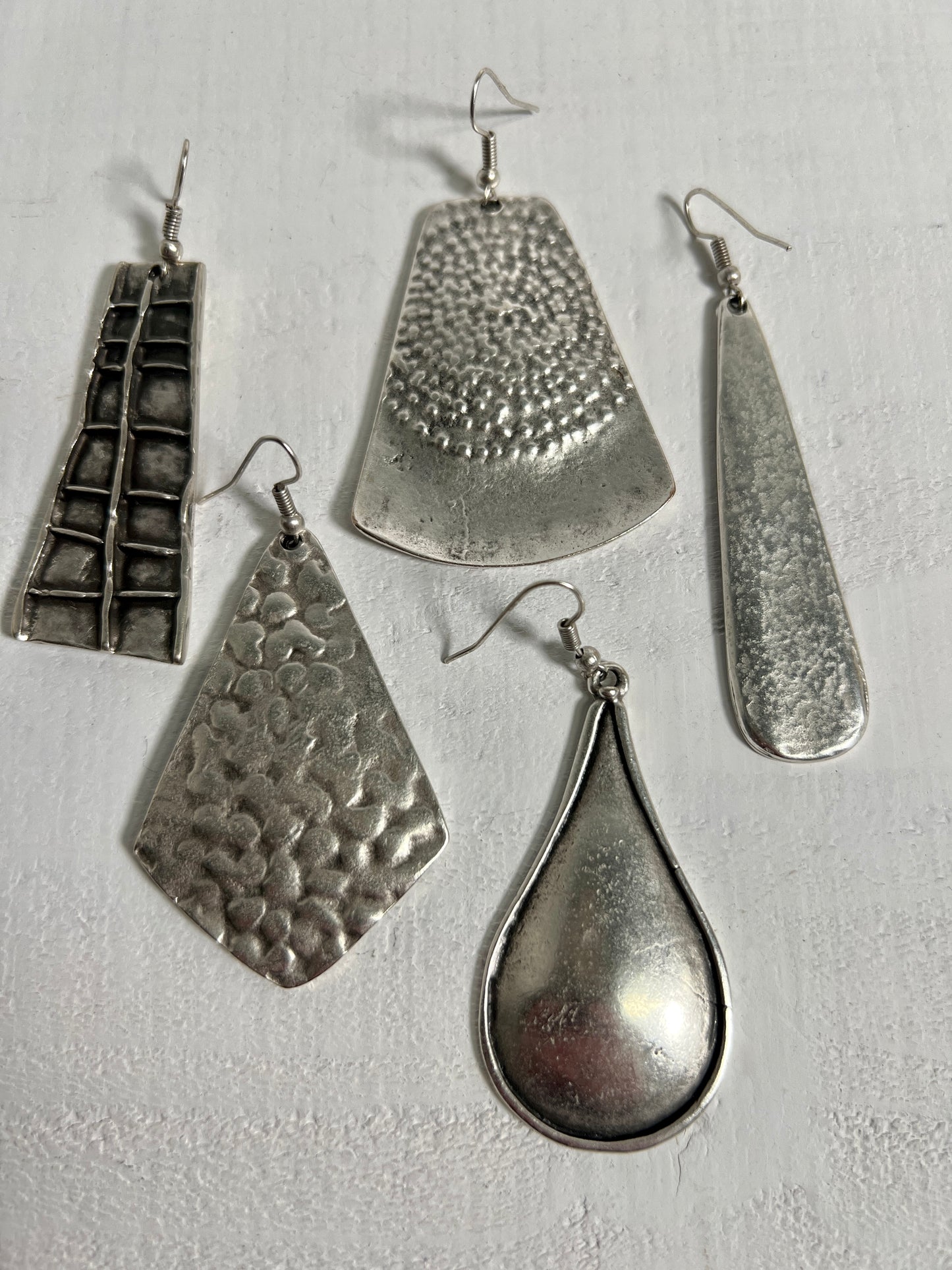 
                  
                    A group of Super Silver Long Boho Statement Earrings on a white surface.
                  
                