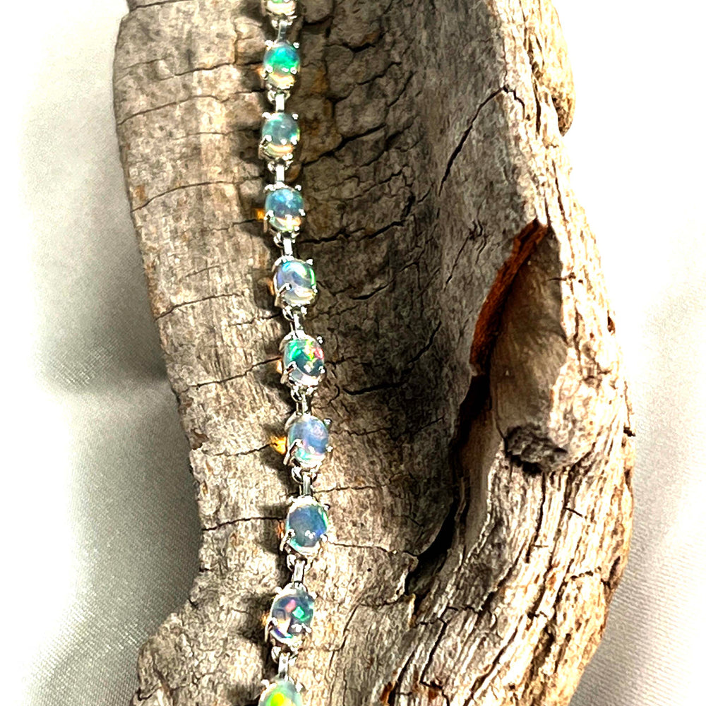 
                  
                    A glamorous Delicate Ethiopian Opal Bracelet adorned with opal stones on a piece of wood, by Super Silver.
                  
                