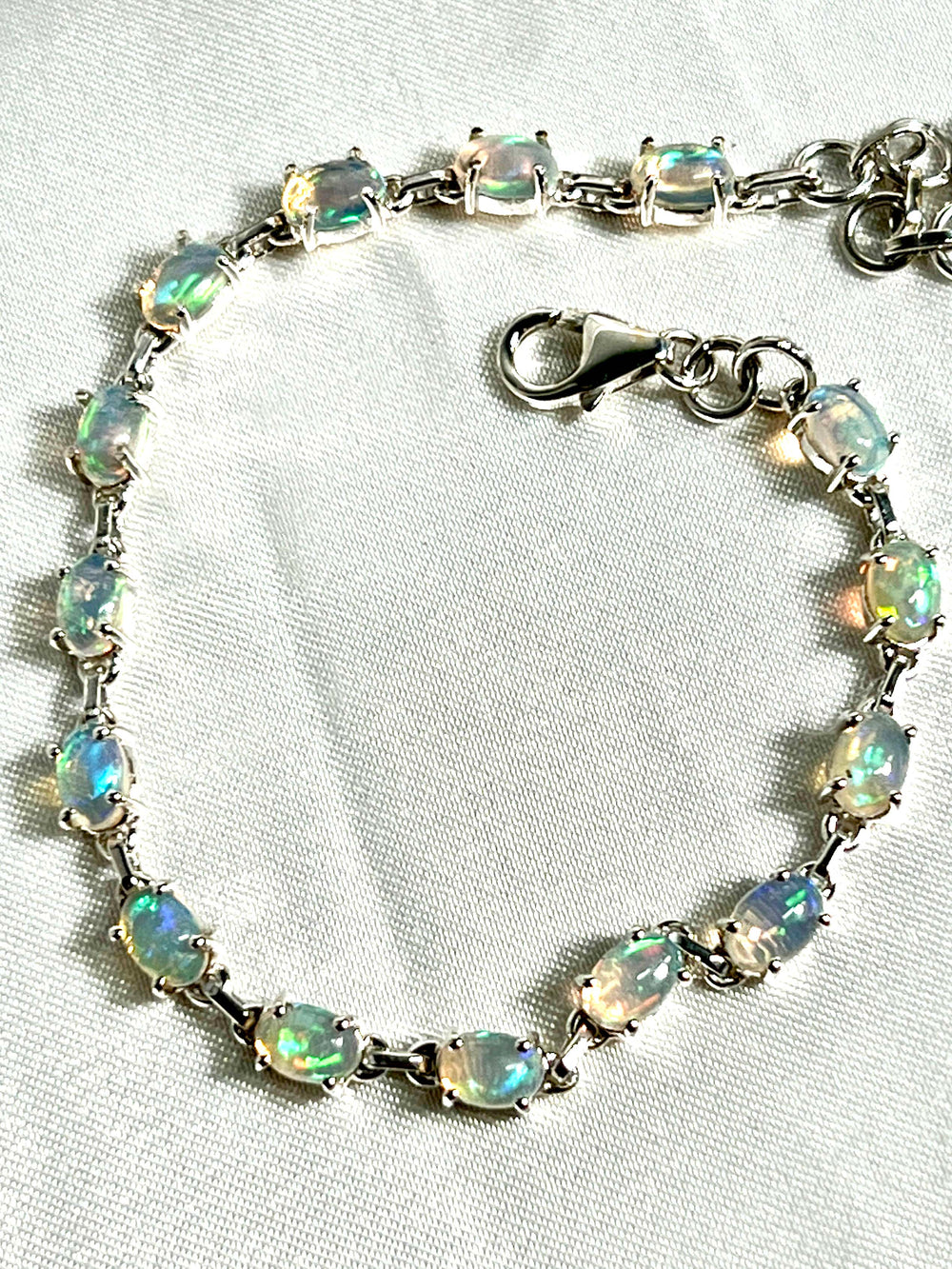 A Super Silver Delicate Ethiopian Opal bracelet exudes glamour as it rests delicately on a pristine white table.