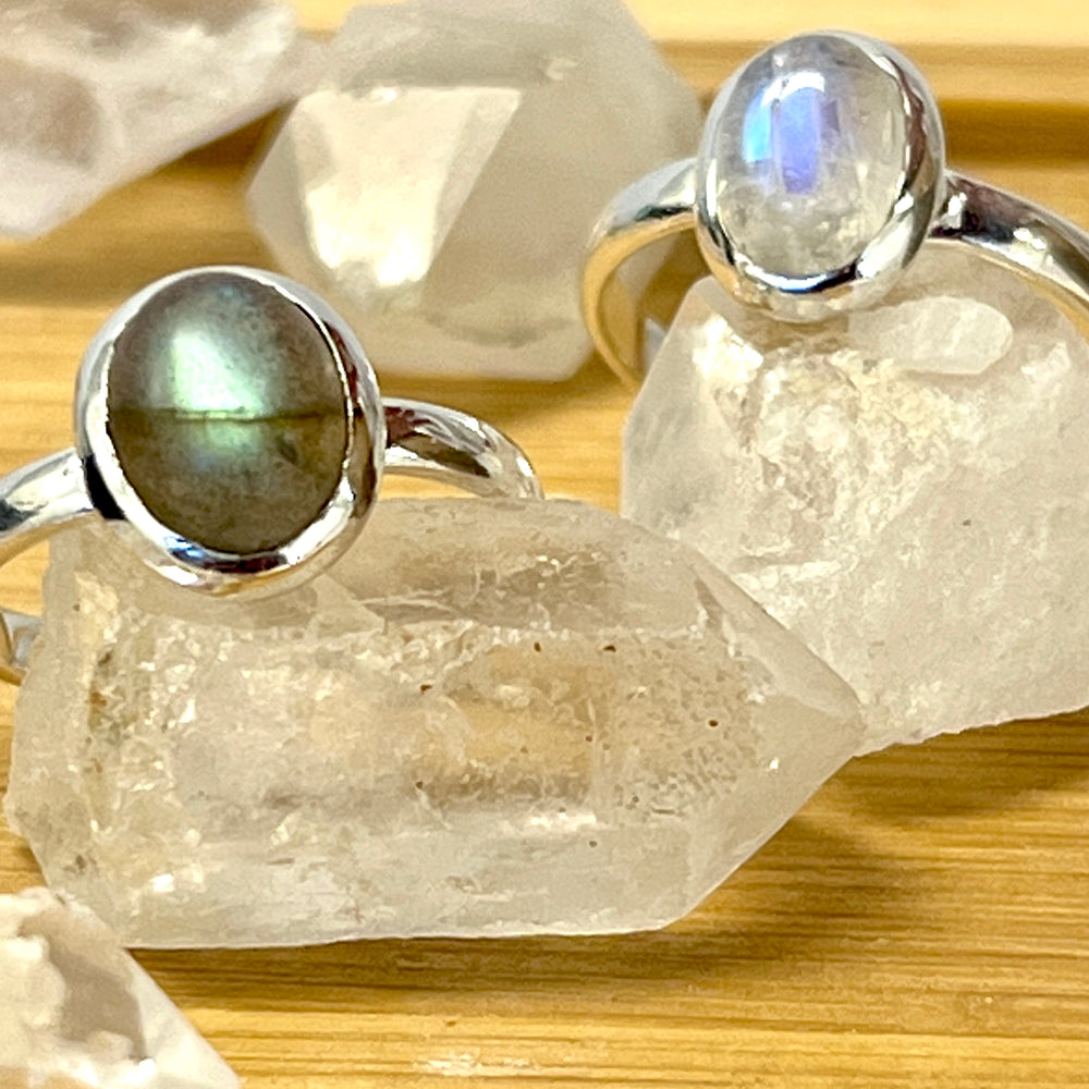 
                  
                    Three Simple Oval Moonstone Or Labradorite Rings with labradorite stones on top of a wooden table.
                  
                