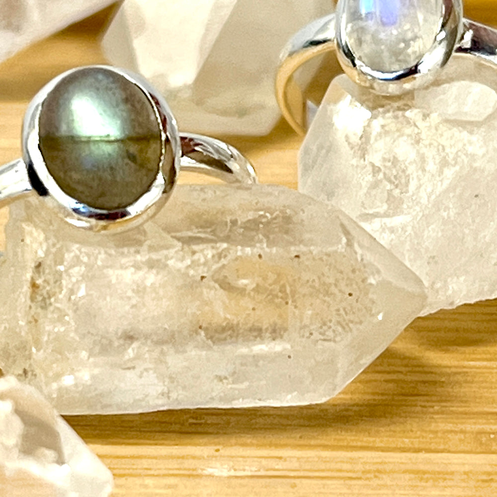 
                  
                    Two simple oval moonstone or labradorite rings set in sterling silver, displayed on a wooden table.
                  
                