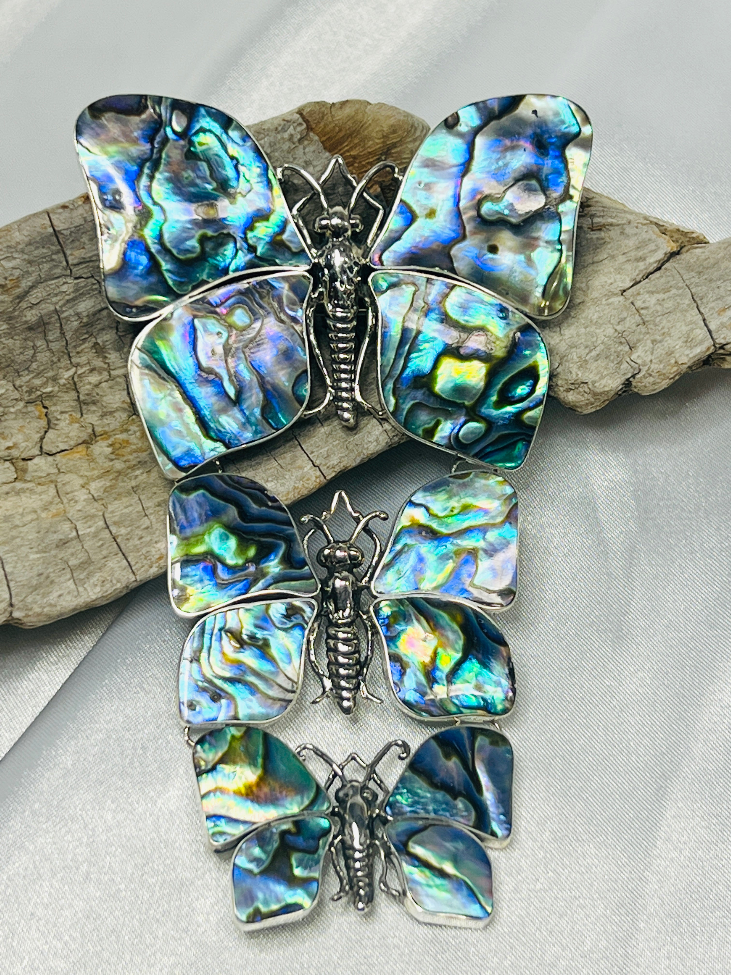 Four Statement Pendants or Brooches with Three Butterflies are displayed on a piece of wood, perfect for any nature lover.