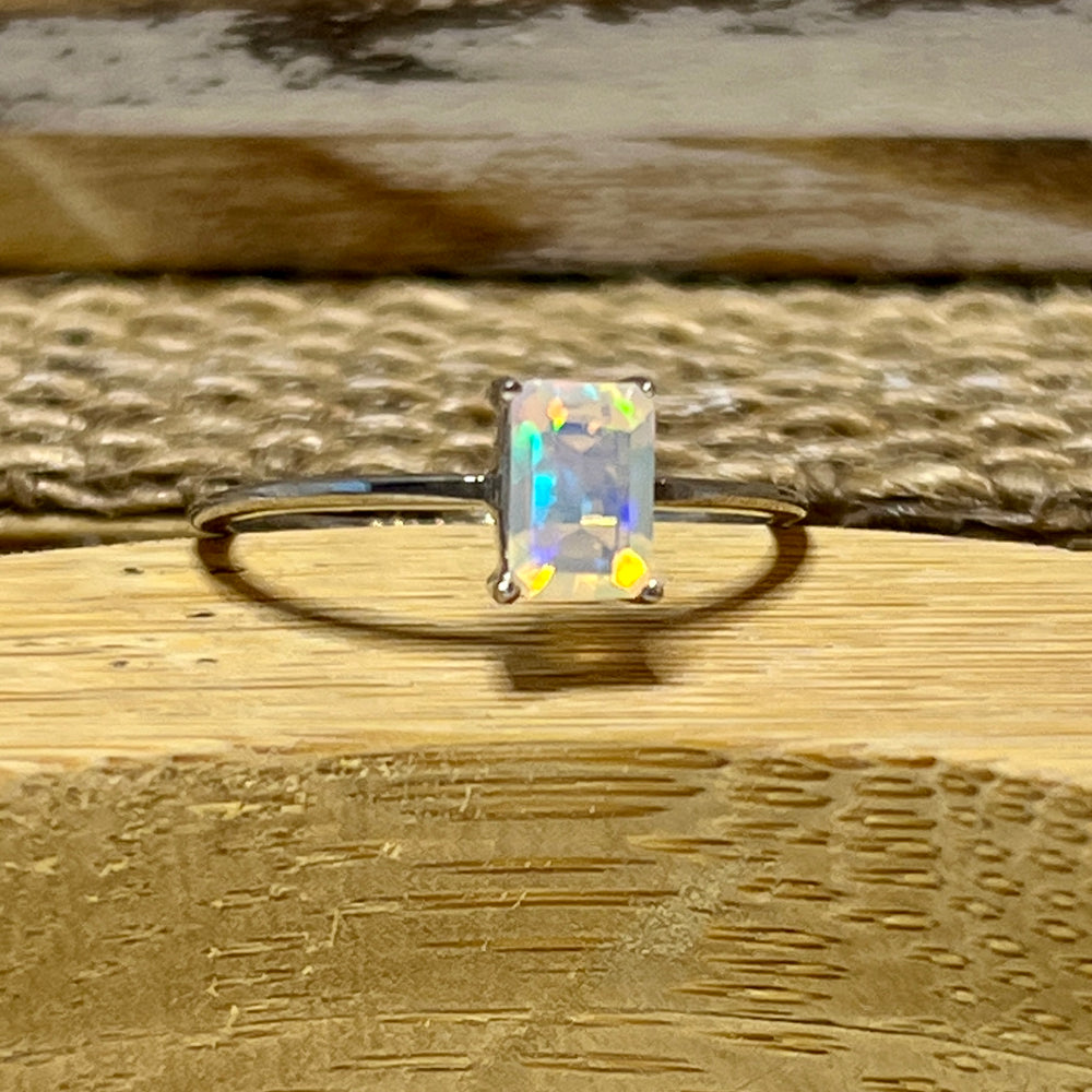 
                  
                    A Cushion Cut Ethiopian Opal ring sitting on top of a wooden table.
                  
                