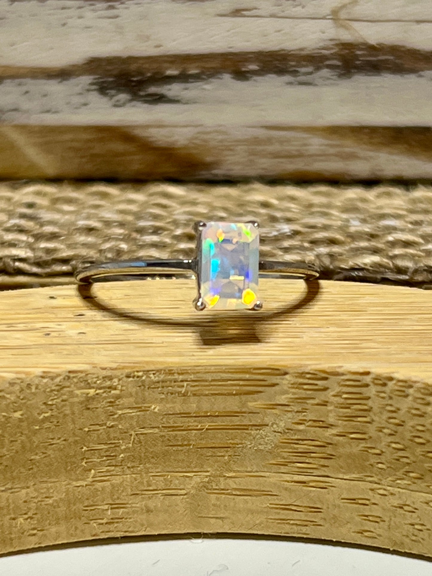 
                  
                    A Cushion Cut Ethiopian Opal ring sitting on top of a wooden table.
                  
                