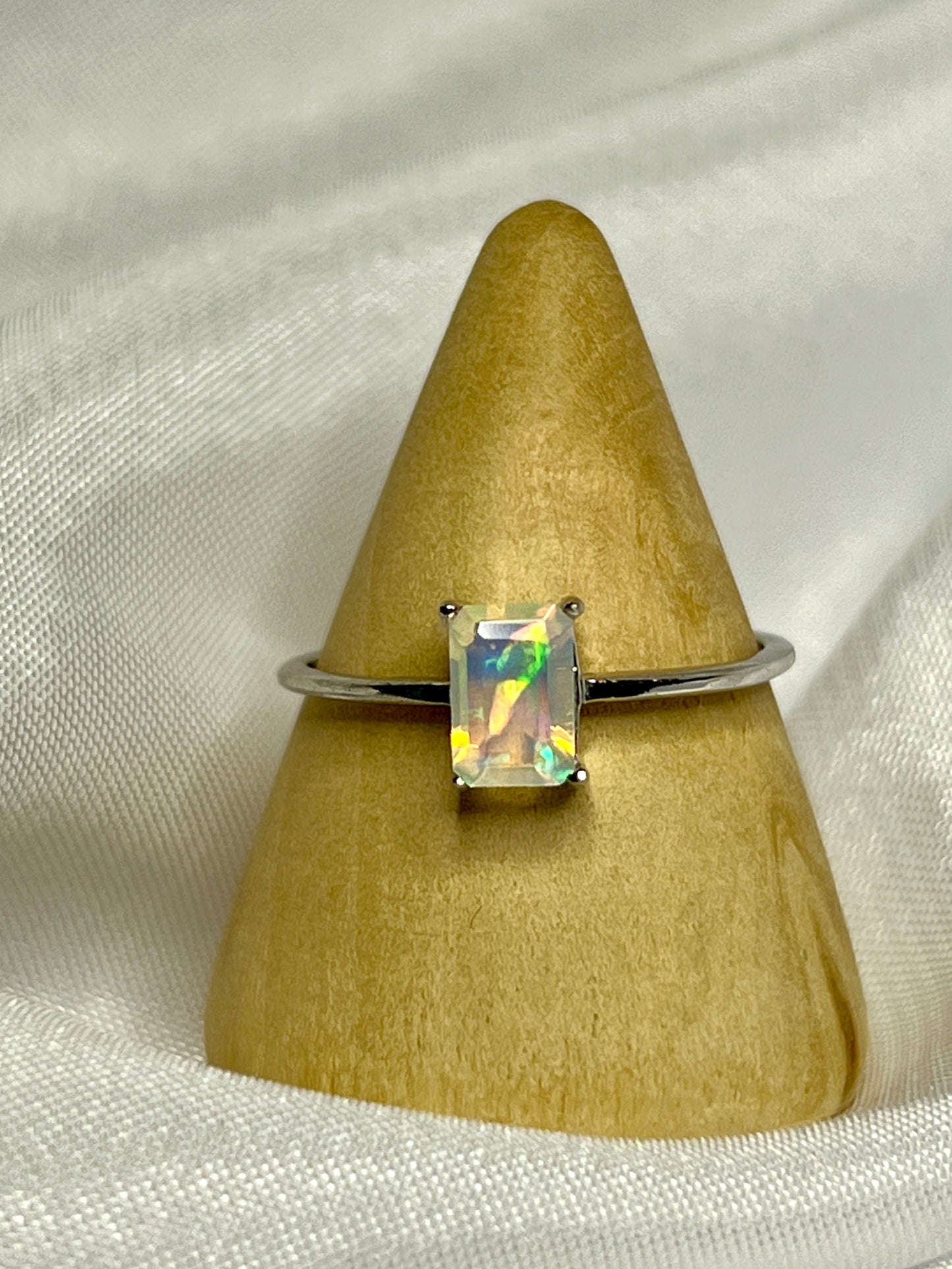 A Cushion Cut Ethiopian Opal engagement ring delicately placed on top of a smooth white cloth.