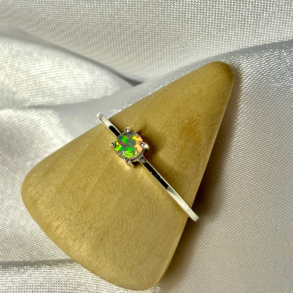 A Dainty Prong Set Facet Cut Ethiopian Opal Ring sitting on top of a piece of cloth.