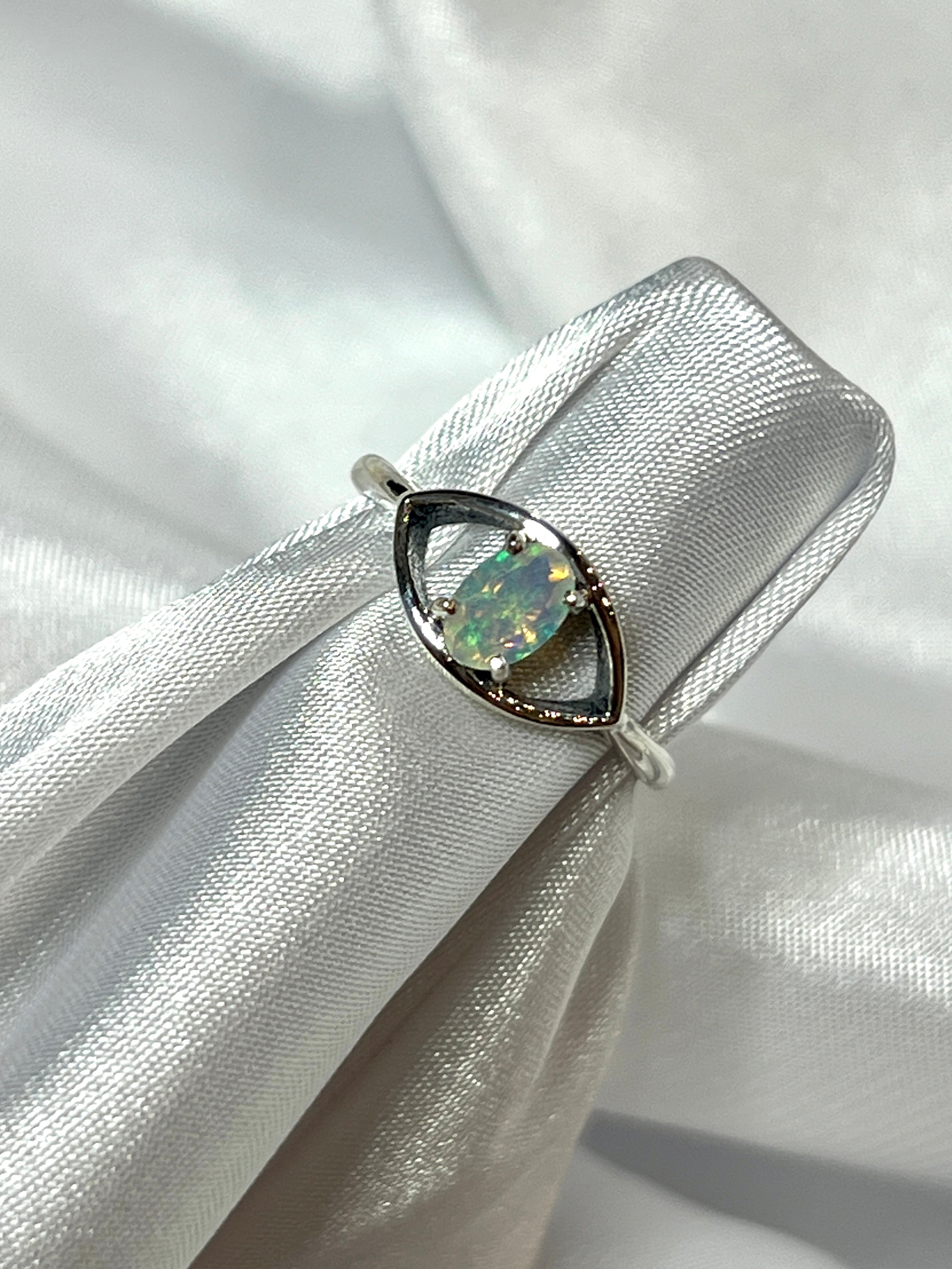 A Facet Cut Ethiopian Opal Evil Eye Ring on a white cloth.