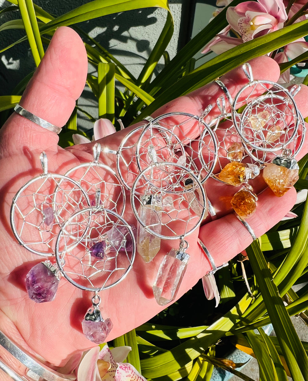 A hand holding a Super Silver Dreamcatcher Pendant with Gemstone Point adorned with raw crystal droplets and gemstones.