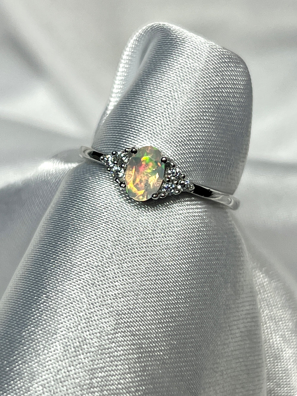 An elegant Ethiopian Opal Ring with Cubic Zirconia Stones on a white cloth.