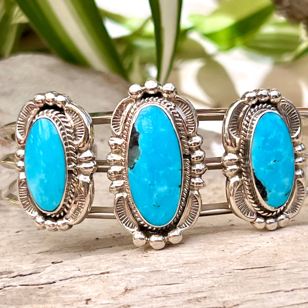A stunning Super Silver Native American Cuff adorned with three turquoise stones, showcasing intricate silverwork.