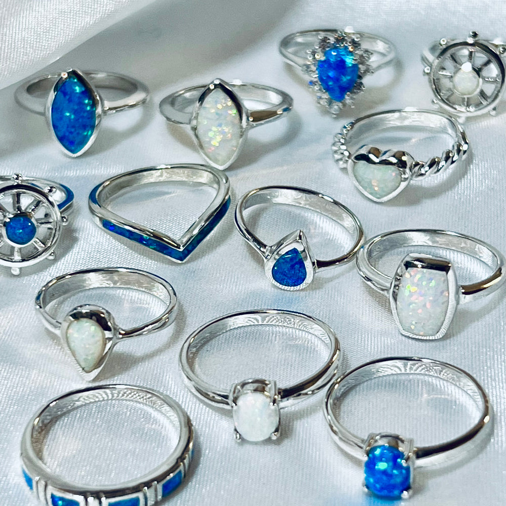 
                  
                    A collection of Elegant Chevron Lab Opal Rings with various blue and opal gemstones, designed for stacking, displayed on a white fabric surface.
                  
                