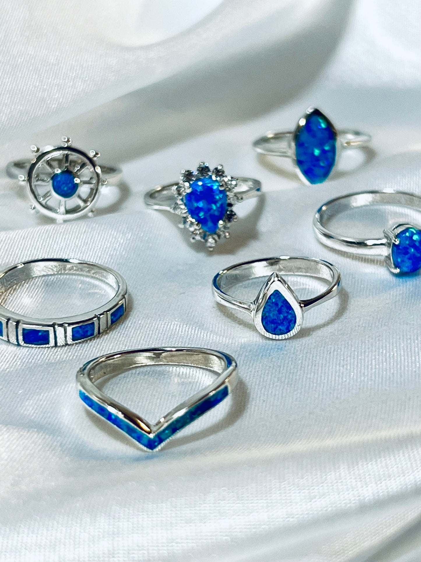 
                  
                    A collection of Elegant Chevron Lab Opal Rings with opal and blue gemstone accents displayed on a white fabric.
                  
                