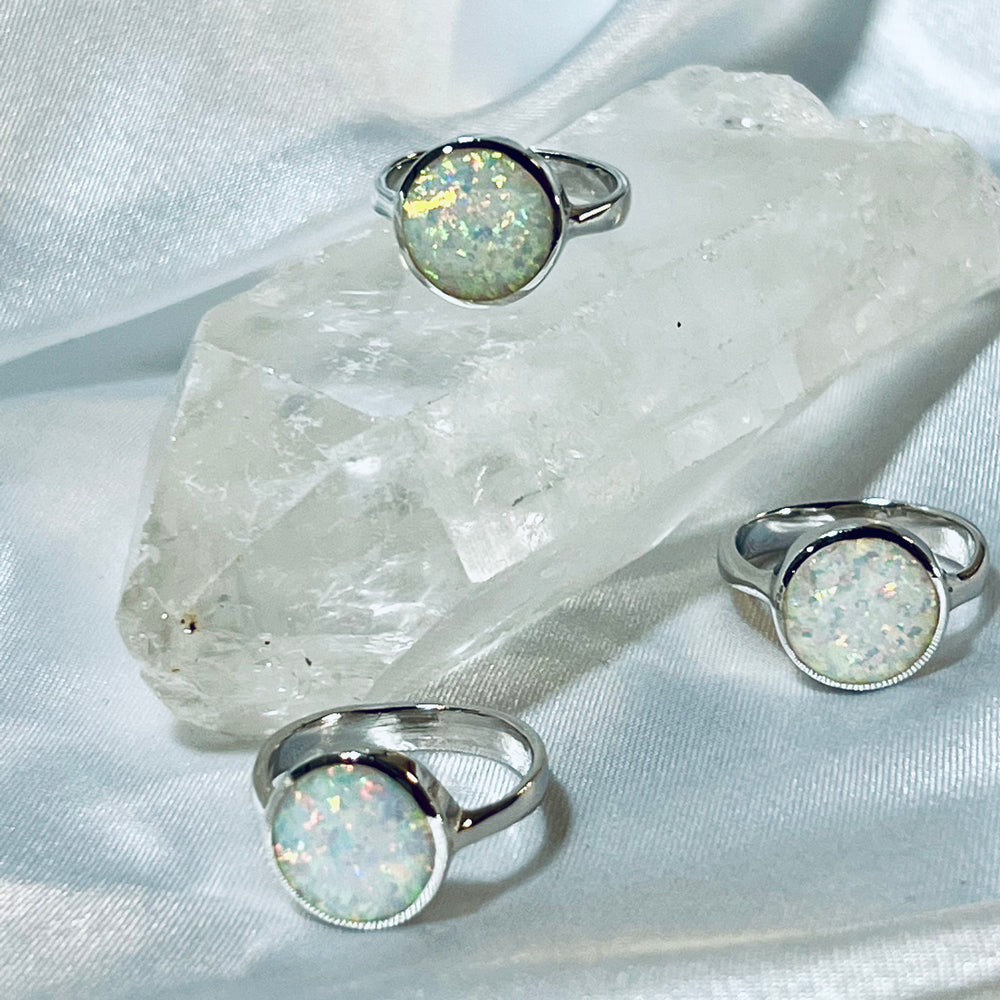 
                  
                    Three Simple Round White Opal Rings displayed on a quartz crystal against a draped fabric background.
                  
                