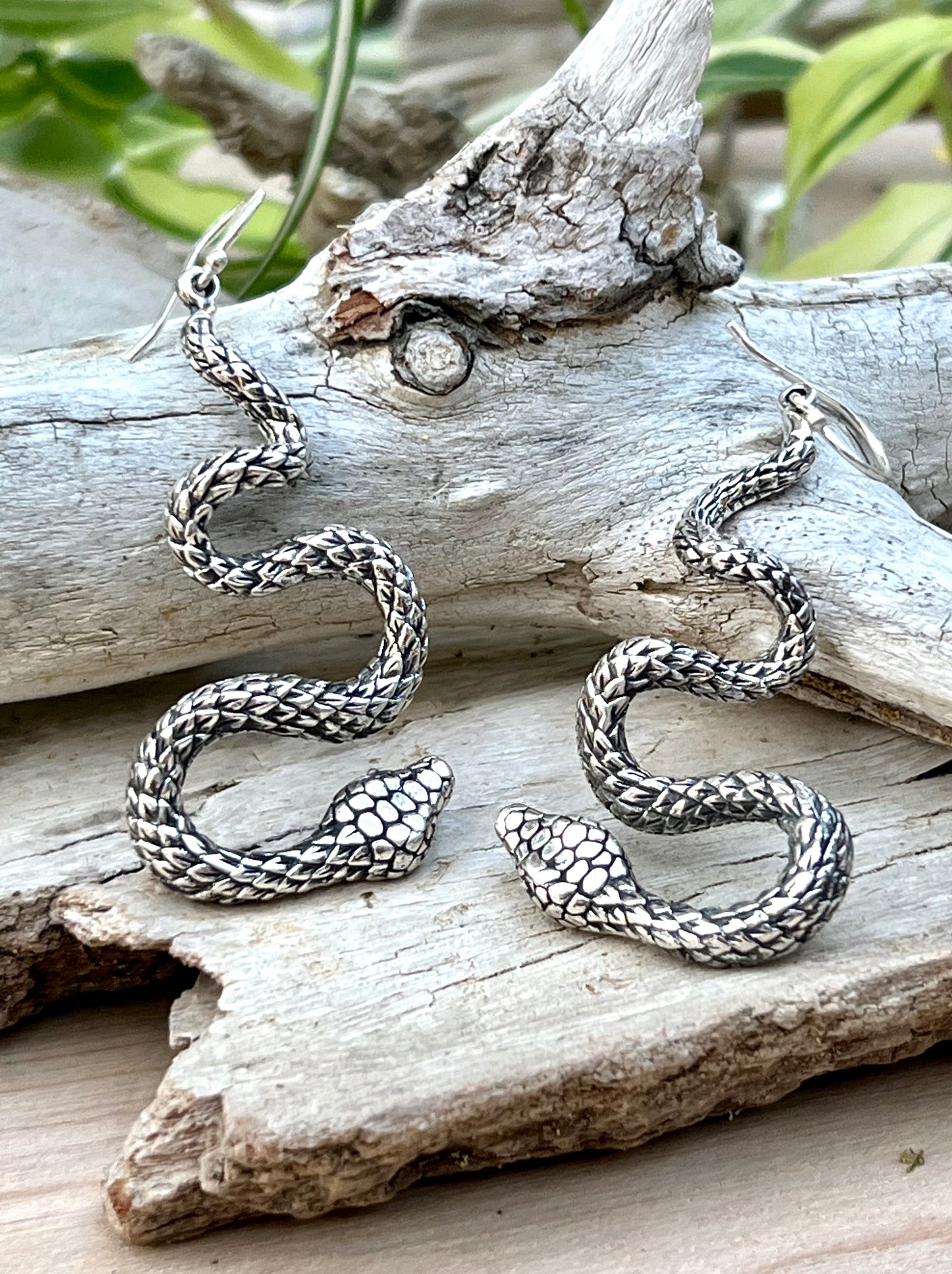 A pair of handcrafted Super Silver Long Twisting Snake Earrings on a piece of wood.