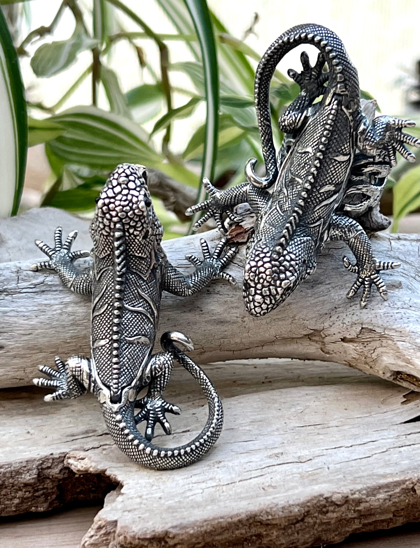 
                  
                    Two Handcrafted Super Silver Iguana Pendants sitting on a piece of wood.
                  
                