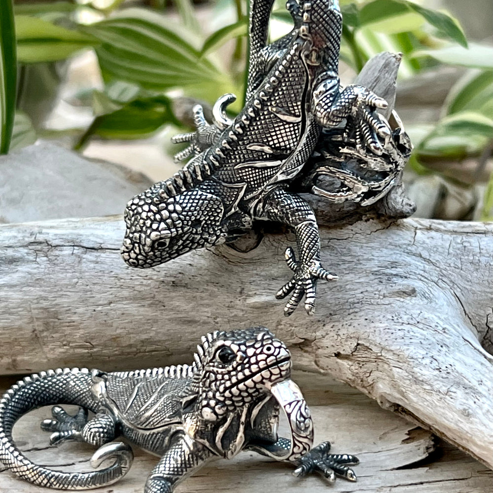 Two Handcrafted Super Silver Iguana Pendants sitting on a piece of wood.
