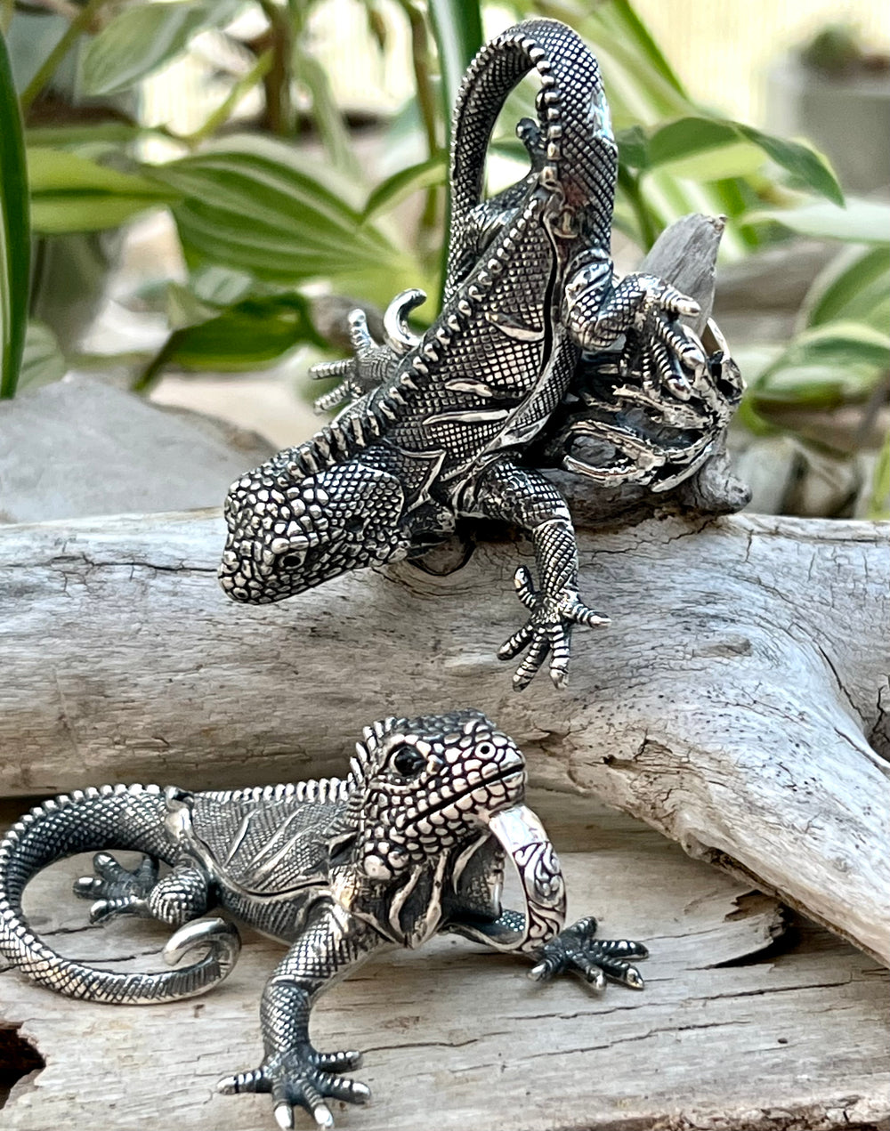 Two Handcrafted Super Silver Iguana Pendants sitting on a piece of wood.