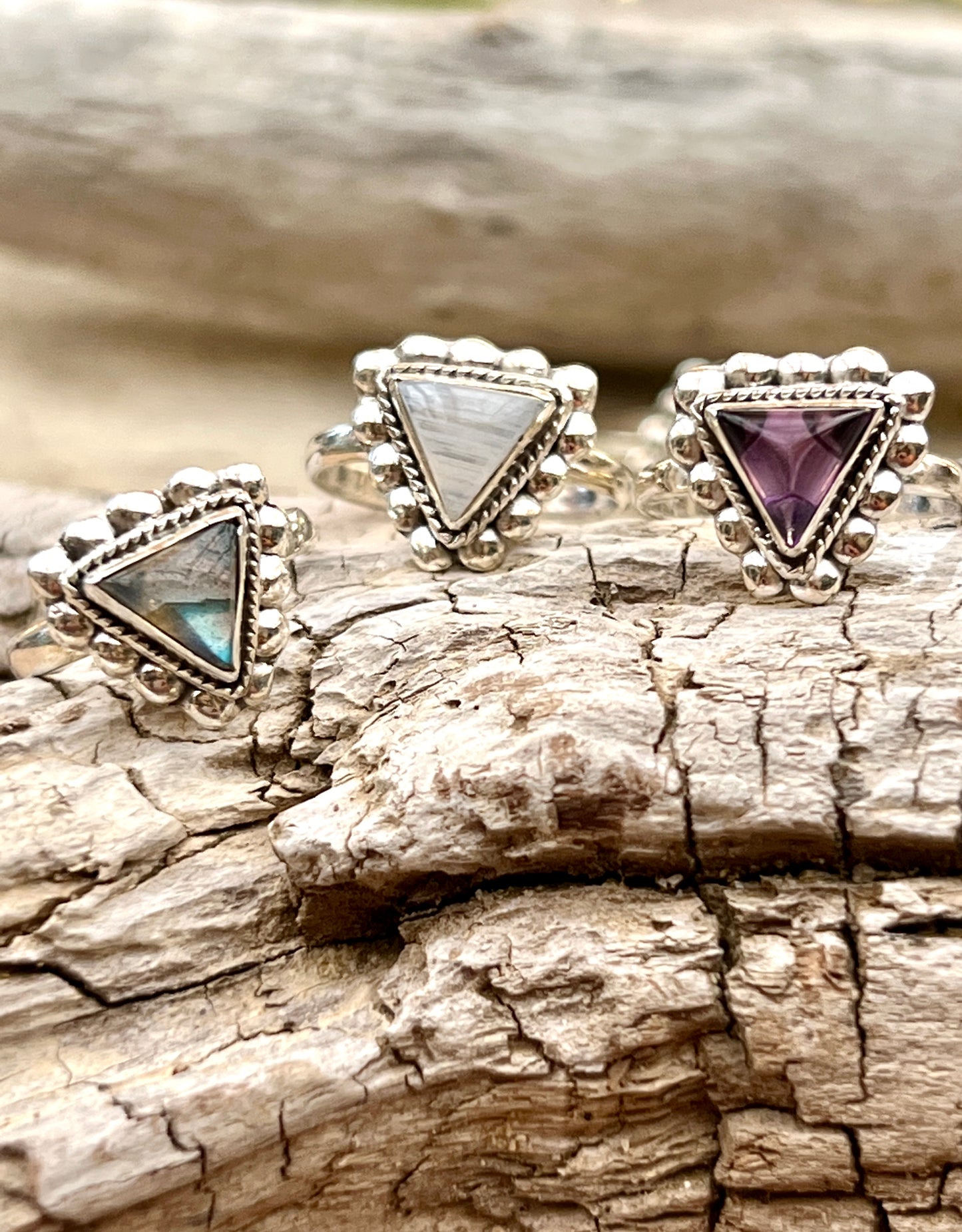 Three Triangle Gemstone Rings with Beads on a piece of wood.