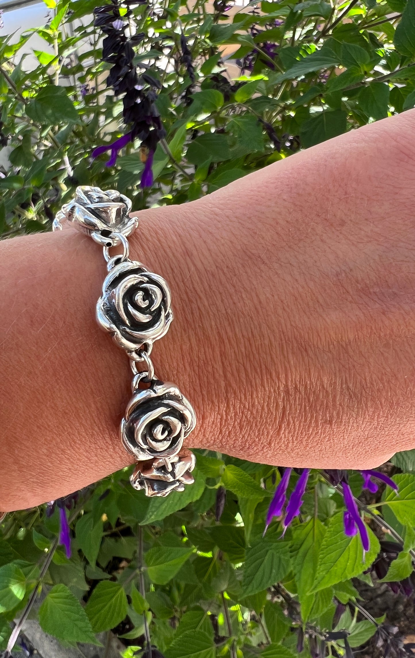 A woman's hand is holding a Super Silver Chic Link Rose Bracelet.