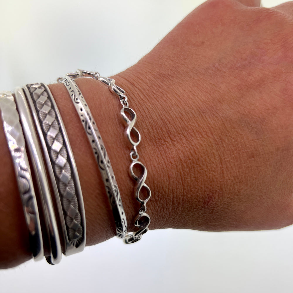 
                  
                    A woman's hand with stacked silver bracelets, including a Super Silver Infinity Sign Link Bracelet and .925 sterling silver pieces.
                  
                