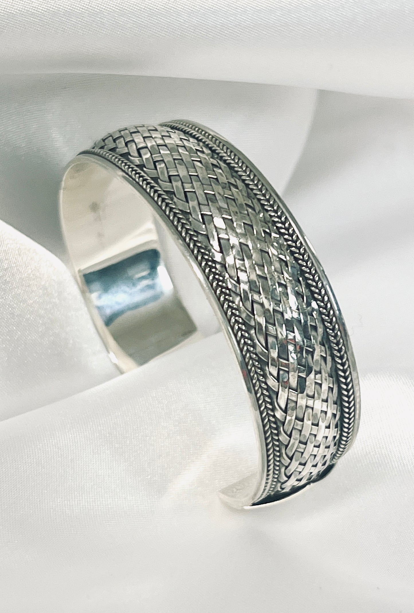 A Super Silver Woven Silver cuff bracelet with an oxidized basket weave design, displayed on a white cloth.
