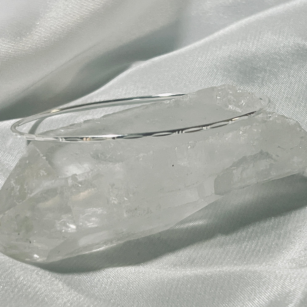 A Delicate Faceted Cut Bangle Bracelet from Super Silver sits on top of a piece of crystal.