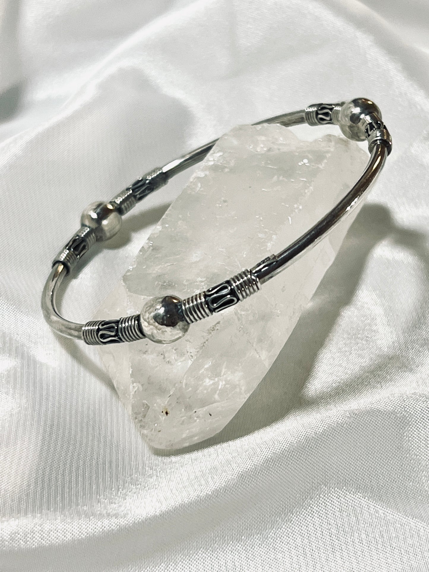 A Super Silver Bali Style Bangle Bracelet sitting on top of a crystal.